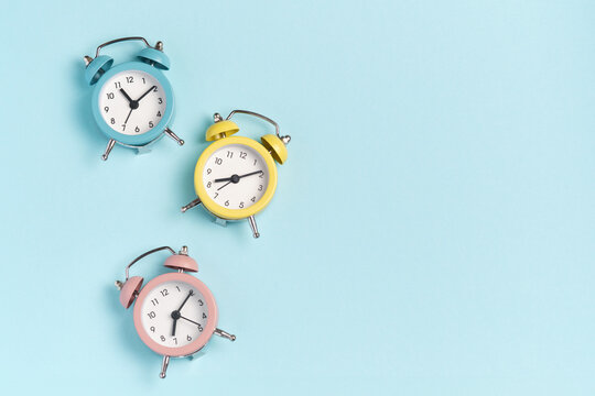 Three alarm clocks of different colors show different times. Start of the day, waking up, morning, different time zones.