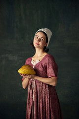 Bakery. Portrait of pretty young woman in image of renaissance maid holding freshly baked bread...