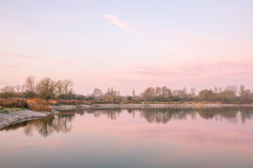 Winter sunrise at Tar Lakes in Oxfordshire, trees reflected in still waters.