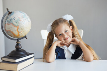 Portrait of beautiful girl in fashion uniform and two ponytails hairstyle sits at a desk on the lesson at school. Cute and pretty caucasian schoolgirl smile and look at the camera. Copy space.