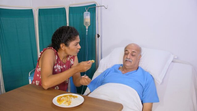 An aged Asian man refusing to eat hospital food - weakness  loss of appetite  boring food  bland food  illness side effects. An Indian daughter feeding her sick father in the hospital - caring fami...