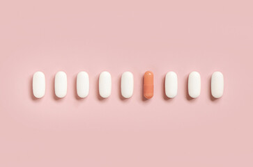 Mix of medical pills with one pink capsule in a line on light pink top view. Dietary supplements