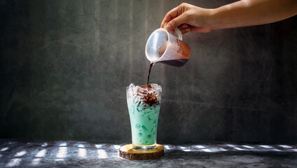 A woman hand  pouring chocolate mixed into mint a glass with an iced menu of mixed cocoa chocolate...