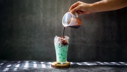 Foto op Canvas A woman hand  pouring chocolate mixed into mint a glass with an iced menu of mixed cocoa chocolate mint drink © NARONG