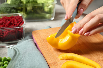 Woman cutting bell pepper and containers with fresh products on table, closeup. Food storage