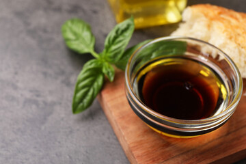 Bowl of organic balsamic vinegar with oil, basil and bread on grey table, closeup. Space for text