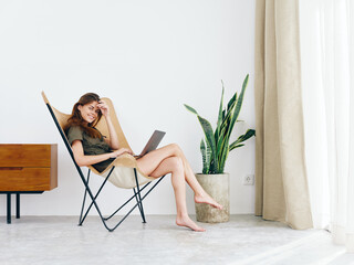 Woman sitting in a chair with a laptop watching a movie and social media at home smile, modern stylish interior Scandinavian lifestyle, copy space.