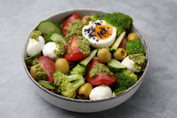 Delicious salad with pesto sauce in bowl on light gray table, closeup