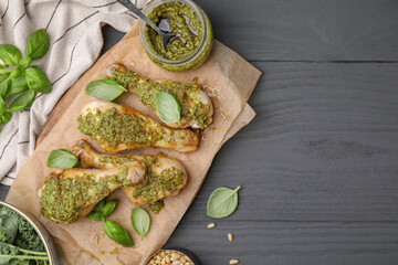 Delicious fried chicken drumsticks with pesto sauce and ingredients on gray wooden table, flat lay. Space for text