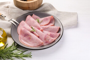 Tasty ham with rosemary and carving fork on white wooden table, space for text