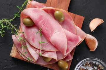 Tasty ham with olives, garlic and thyme on black textured table, flat lay