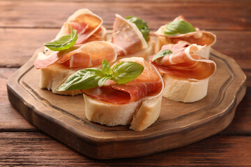 Board of tasty sandwiches with cured ham and basil leaves on wooden table, closeup