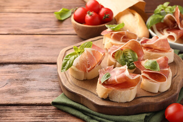 Tasty sandwiches with cured ham, basil leaves and tomatoes on wooden table. Space for text