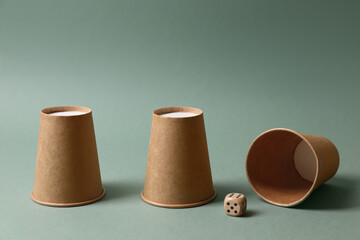 Three paper cups and dice on pale olive background. Thimblerig game