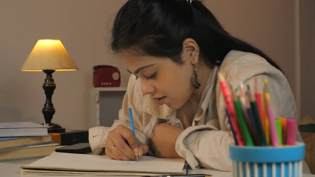 A serious Indian writing on a piece of paper - education concept  nighttime study  college assignment. A young Indian woman completing college work - completing home work  preparing for exams  and ...