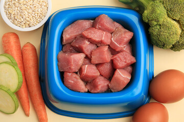 Raw meat in bowl and healthy products for pet on beige background, flat lay