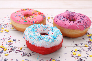 Glazed donuts decorated with sprinkles on white wooden table, closeup. Tasty confectionery