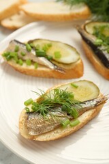 Delicious sandwiches with sprats, pickled cucumber, green onion and dill on plate, closeup