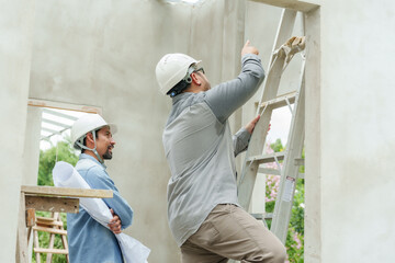 Asian construction supervisor Climb the ladder and point out the problem area. Consultation of a bearded Indian engineer wearing a helmet. Let workers rush to build houses in the construction area.