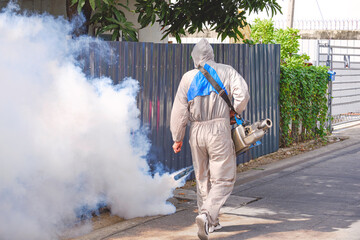 Rear view of healthcare worker in protective clothing using fogging machine spraying chemical to...