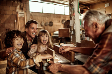 Grandfather carpenter teaching his son and grandchildren how to work with wood in a wood workshop