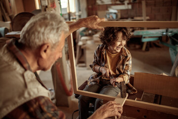 Grandfather carpenter teaching his grandson how to work with wood in a wood workshop