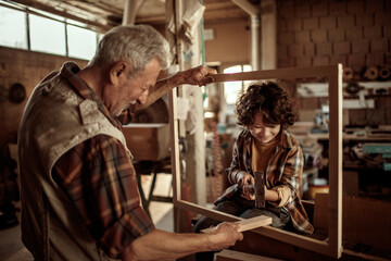 Grandfather carpenter teaching his grandson how to work with wood in a wood workshop