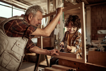Grandfather carpenter teaching his grandson how to work with wood in a wood workshop