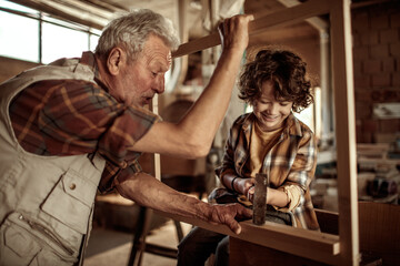 Grandfather carpenter teaching his grandson how to work with wood in a wood workshop