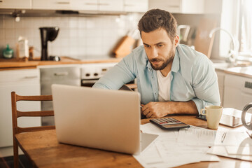 Worried young Caucasian man going over his bills and home finances in the morning in the kitchen