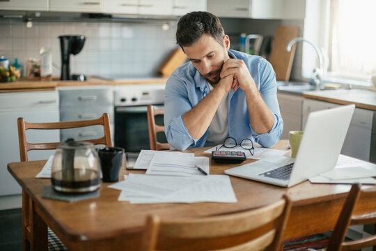 Worried young Caucasian man going over his bills and home finances in the morning in the kitchen