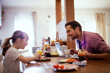 Fototapeta na wymiar Young single father having fun and eating breakfast with his daughter in the kitchen
