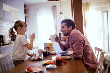 Happy young single father eating breakfast with his daughter in the kitchen