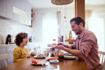 Happy young single father having breakfast with his son in the morning in the kitchen