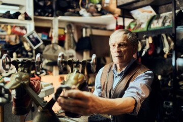 Senior male cobbler restoring a shoe in his old workshop in the city