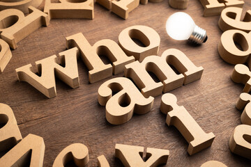 Who Am I, identity question by thick wooden alphabets with light source from a glowing bulb