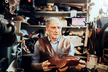 Fototapeta na wymiar Senior male cobbler restoring a shoe in his old workshop in the city