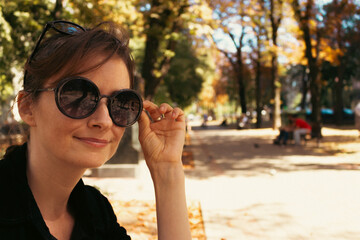 Girl in sunglasses on the bench in park. Attractive woman in autumn alley. Woman portrait in sunglasses. Fall in downtown. Street lifestyle. Daily life in big city. Free in expressions.