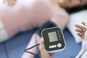 Doctor measuring senior female patient's blood pressure in examination room at hospital.