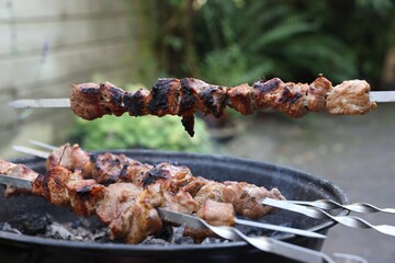 Cooking delicious kebab on metal skewers outdoors
