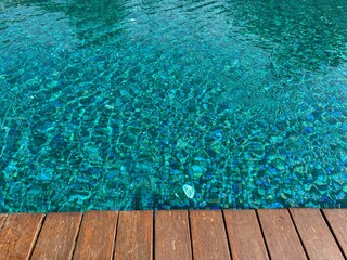 Clear rippled water in swimming pool and wooden deck outdoors. Space for text