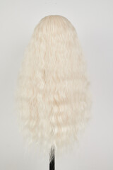 Natural looking blonde wig on white mannequin head. Long hair on the plastic wig holder isolated on white background, back view.