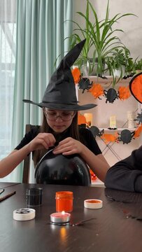 happy children in witch costumes are getting ready to celebrate Halloween, inflate balloons in black and orange, two girlfriends decorate the room for Halloween