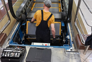Man repairs escalator, steps inside, standing with her back near the step, tools are.