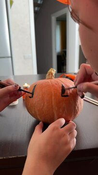 children are preparing for the Halloween holiday, paint a scary face on a pumpkin with brushes for home decoration, girls decorate a pumpkin for Halloween