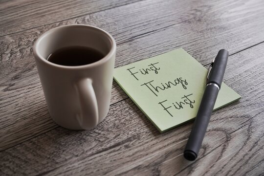Closeup image of cup of coffee, pen and notepad with text FIRST THINGS FIRST.