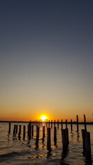 Obraz premium The sun's warm rays dance across the waves as it slowly dips below the horizon, casting a golden glow over the beach..