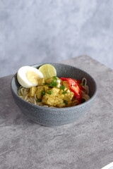noodles topped with boiled egg, spring onions, fried onions, dumplings, lime