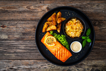 Grilled salmon steak with baked potatoes and sauerkraut served on wooden table 