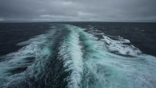 Side view along ship. Wind blows spray off wave. Wind breaks waves with white foam.
